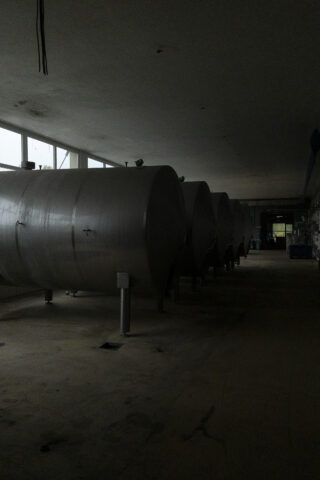In einer schwach beleuchteten Industrieanlage steht eine Reihe großer, zylindrischer Lagertanks aus Metall.