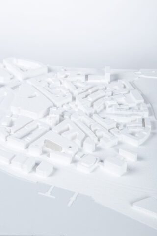 Ein weißes Architekturmodell zeigt einen Stadtplan mit verschiedenen Gebäuden und Straßen, die in einem dichten, geordneten Muster angeordnet sind.
