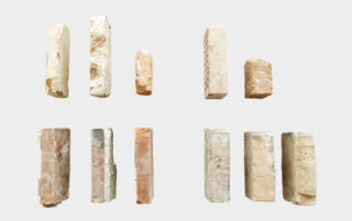 Zehn rechteckige Stein- oder Ziegelstücke unterschiedlicher Farbe und Struktur sind in zwei Reihen auf einem schlichten weißen Hintergrund angeordnet.