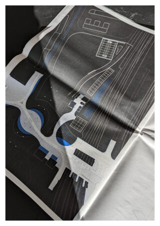 Ein gedruckter architektonischer Lageplan mit weißen und blauen Linien und Formen auf schwarzem Hintergrund, auf einer flachen Oberfläche ausgebreitet.