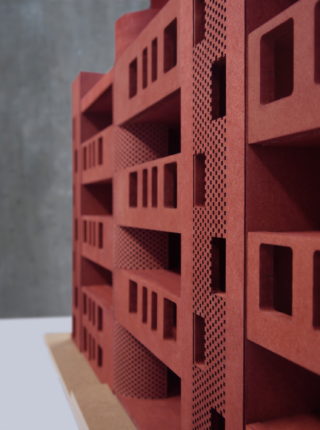 Eine Nahaufnahme eines roten Architekturmodells mit mehreren rechteckigen Fenstern und perforierten Fassadenplatten.