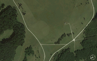 Luftaufnahme von Grasfeldern, die von weißen Pfaden durchzogen sind, Waldgebieten an den Rändern und einer kleinen kreisförmigen Lichtung in der Nähe der Mitte.