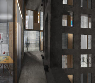 Das Innere eines Betongebäudes mit mehreren quadratischen Fenstern, Glasbausteinen und einem Arbeitsbereich mit Schreibtisch, Lampe und Kunstbedarf, der durch ein Fenster sichtbar ist.