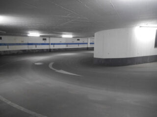 Eine geschwungene Rampe in einem Parkhaus mit aufgemalten Richtungspfeilen und nummerierten Parkplätzen entlang der Wand.