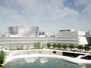 Ein moderner Gebäudekomplex mit der Aufschrift „Berlin-Tegel“ mit großen Glasfenstern, umgeben von Bäumen und einem Teich, vor der Kulisse einer urbanen Skyline.