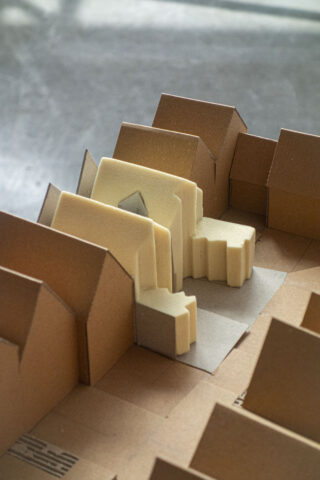 Eine Nahaufnahme eines Architekturmodells aus Pappe und Schaumstoff, das eine Ansammlung von Gebäuden zeigt, die in einem städtischen Grundriss angeordnet sind.