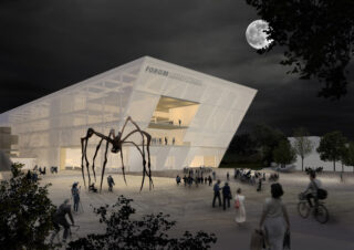 Modernes, eckiges Gebäude mit der Aufschrift „Forum Unimahall“ bei Nacht, mit Menschen, die sich draußen versammelt haben, und einer großen Spinnenskulptur auf dem Platz; Vollmond am Himmel.