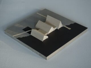 Ein kleines Architekturmodell mit drei Giebelholzkonstruktionen auf quadratischem Sockel, mit kontrastierenden hellen und dunklen Flächen und einem schmalen Diagonalstreifen.
