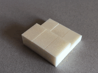 Auf einer schlichten, braunen Fläche liegen zwei rechteckige Schaumstoffblöcke mit sichtbaren Schnittlinien.