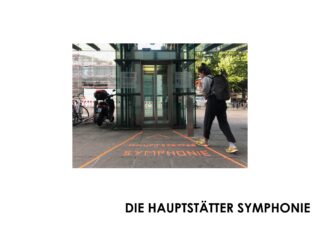 Vor dem Eingang eines Glasgebäudes läuft eine Person über orangefarbenes Band auf dem Bürgersteig mit der Aufschrift „HAUPTSTÄTTER SYMPHONIE“.