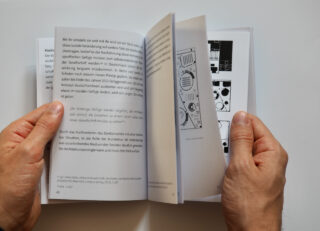 Eine Person hält ein Buch in der Hand und blättert darin. Dabei kommen Seiten mit Text und eine Teilseite mit Schwarzweißdiagrammen oder -illustrationen zum Vorschein.