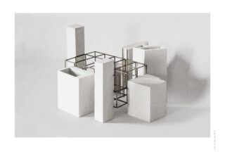 Eine minimalistische Skulptur aus weißen rechteckigen Blöcken und einer Metallgitterstruktur, angeordnet auf einem schlichten weißen Hintergrund.