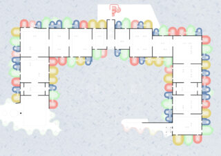 Grundriss eines Gebäudes mit L-förmigem Grundriss, mehreren Räumen entlang des Umfangs und farbigen halbkreisförmigen Formen, die die Außenwände umreißen.