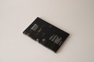 Auf einem weißen Untergrund liegt geschlossen ein schwarzes Taschenbuch mit dem Titel „Sammelbände – Series Bundles“, auf dem Cover sind weißer Text und eine schwache Stadtlandschaft zu sehen.