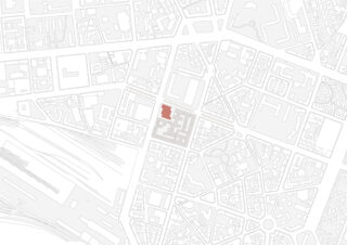 Ein Stadtplan mit grau umrandeten Gebäuden; ein Block ist beige hervorgehoben und ein bestimmtes Gebäude darin ist rot schattiert.