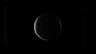 Eine dunkle, teilweise beleuchtete Kugel ist vor einem schwarzen Hintergrund zentriert und ähnelt einer Mondsichel oder einem Planeten im Schatten.