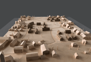 Ein hölzernes Architekturmodell zeigt den Grundriss einer Kleinstadt mit Gebäuden, Straßen und Freiflächen auf neutralem Hintergrund.