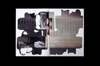 Eine aufgeschlagene Zeitschrift zeigt abstrakte schwarze und graue Formen und Texturen, die sich über beide Seiten auf einem weißen Hintergrund überlappen.