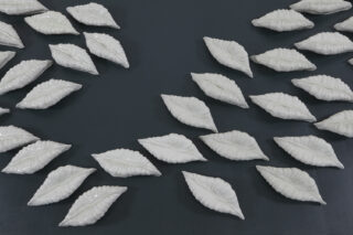 Dutzende weißer Keramikskulpturen in Lippenform sind in Gruppen auf einer dunklen Oberfläche angeordnet.