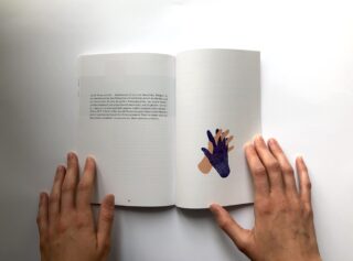 Die Hände einer Person halten ein Buch offen; die linke Seite enthält Text und die rechte Seite zeigt eine Abbildung zweier sich überlappender Hände.