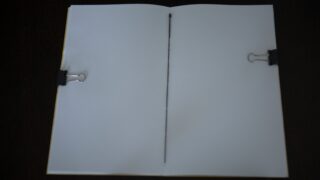 Ein offenes, leeres Notizbuch, das vor einem dunklen Hintergrund von zwei Heftklammern (eine auf jeder Seite) flach gehalten wird.