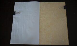 Ein geöffneter Ordner mit zwei Blättern Papier, einem weißen und einem beigefarbenen, die jeweils mit einer schwarzen Büroklammer befestigt sind, liegt auf einer dunklen Oberfläche.