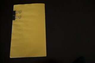 Ein geschlossener gelber Ordner wird mit einer schwarzen Büroklammer befestigt und auf eine dunkle Oberfläche gelegt.