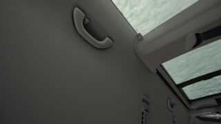 Blick auf die Innendecke eines Autos mit einem Haltegriff, einem Teil eines Schiebedachs und Regentropfen auf der Scheibe.