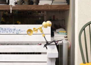 Vor einem Schaufenster mit Regalen und verschiedenen Artikeln darin ist ein gelbes Anemometer an der Kante einer weißen Holzbank befestigt.