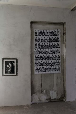 An einer rauen, unfertigen Wand neben einer Tür hängt ein Graustufenfoto, das mit Reihen abstrakter schwarzer geometrischer Formen auf weißem Hintergrund bedeckt ist.