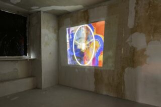 Ein farbenfrohes abstraktes Kunstwerk wird auf die Wand eines unfertigen Betonraums mit kahlen Wänden und einem abgedeckten Fenster projiziert.