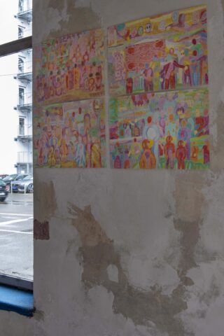 Zwei farbenfrohe, abstrakte Gemälde mit menschenähnlichen Figuren hängen an einer abgenutzten, strukturierten Wand in der Nähe eines Fensters mit Blick auf einen Parkplatz.