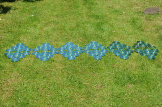 Blaugrüne geometrische Objekte, die bei Tageslicht in einem symmetrischen Muster auf einer Rasenfläche angeordnet sind.