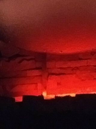 Rot-oranges Licht beleuchtet eine raue Ziegel- oder Steinwand mit sichtbaren Rissen und unebenen Oberflächen.