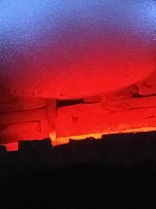 Rot glühende Ziegel sind in einem scheinbaren Brennofen oder Ofen gestapelt, und ein helles orangerotes Licht erhellt die Szene.