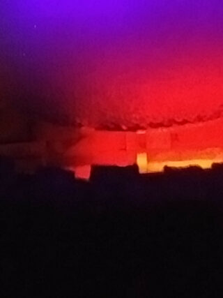 Farbverlaufslichter in Lila, Rot und Orange beleuchten eine abstrakte, strukturierte Oberfläche mit einem dunklen Bereich am unteren Bildrand.