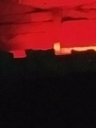 Unten erscheint die dunkle Silhouette einer unebenen Oberfläche, darüber ein rot und orange beleuchteter, strukturierter Hintergrund.