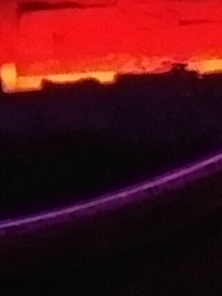 Unscharfes Bild mit einem leuchtend roten und orangefarbenen Bereich oben, einem dunklen Mittelteil und einer gebogenen violetten Linie weiter unten.