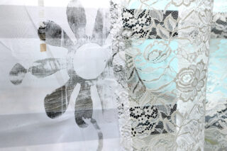 Nahaufnahme zweier überlappender Stoffe: einer mit einem großen schwarzen Blumendruck auf durchsichtigem weißen Material und der andere mit zarten, komplizierten weißen Spitzenmustern.