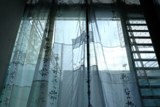 Vor einem großen Fenster hängen transparente, gemusterte Vorhänge, die viel Licht in den Raum lassen.