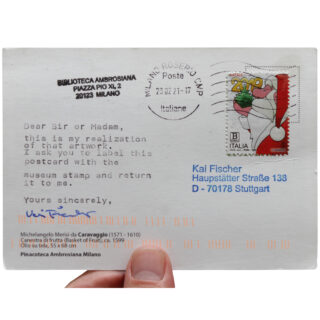 Eine Hand hält eine an Kai Fischer in Stuttgart adressierte Postkarte mit italienischer Briefmarke, Poststempel und einer gedruckten Nachricht mit der Bitte um Beschriftung und Rücksendung der Postkarte.