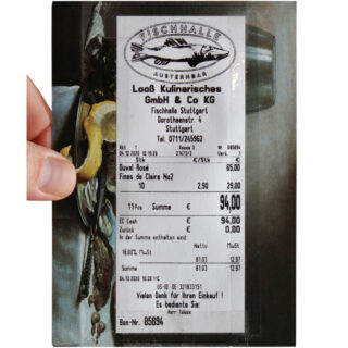 Eine Hand hält eine Quittung der Fischhalle Stuttgart, auf der Meeresfrüchte und Preise aufgelistet sind. Im Hintergrund ist ein Gemälde mit Meeresfrüchte-Motiven zu sehen.