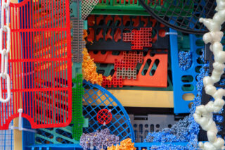 Eine Nahaufnahme verschiedener bunter Kunststoffgitter, Schaumstoffperlen und strukturierter Materialien, die in einer abstrakten Anordnung übereinander angeordnet sind.