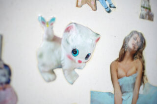 Auf einer weißen Fläche sind ein Aufkleber eines weißen Cartoon-Kätzchens mit blauen Augen und ein Fotoausschnitt einer Frau in einem trägerlosen Kleid angebracht.