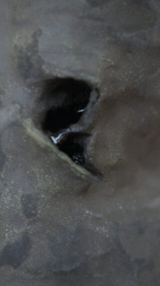 Eine Nahaufnahme einer rauen, grauen Oberfläche mit einem kleinen, dunklen Loch oder Hohlraum in der Mitte, der eine glänzende Flüssigkeit enthält.