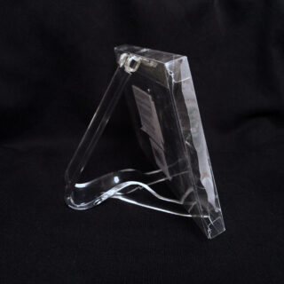 Ein durchsichtiger Bilderrahmen aus Kunststoff steht auf einer schwarzen Oberfläche und wird von einem transparenten hinteren Bein im Staffelei-Stil getragen.