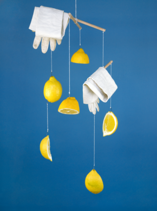 Ein Mobile aus Gummihandschuhen und Zitronenhälften, die an Schnüren vor blauem Hintergrund hängen.