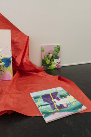 Mehrere abstrakte Gemälde sind auf und um ein rotes Laken herum ausgestellt, das vor einer weißen Wand auf einem dunklen Boden hängt.