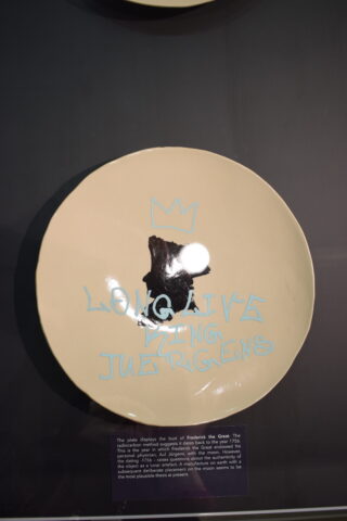 Ein Keramikteller mit einer schwarzen Büstensilhouette, einer blauen Krone und den in Blau geschriebenen Worten „LANG LEBE KÖNIG JÜRGENS“.