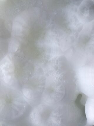 Nahaufnahme einer durchscheinenden weißen Mineraloberfläche mit wolkigen, kristallinen Mustern und subtilen Texturen.